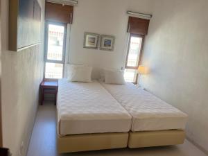 Un dormitorio con una gran cama blanca con dos ventanas. en Armação de Pêra - Beach Apartment - Sea View- Walk to the Beach - Algarve, en Armação de Pêra
