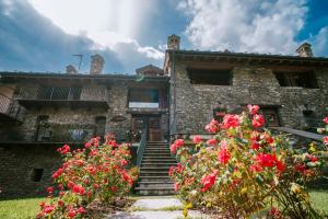 ニュスにあるMaison Rosset agriturismo, CAMERE, appartamenti e spa in Valle d'Aostaの赤い花の古い石造りの建物