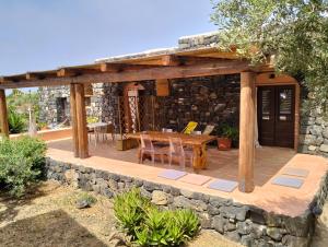 een houten terras met een tafel en een stenen muur bij Dammusielenas in Pantelleria
