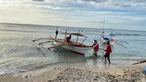 a group of people standing next to a boat on the beach at Talim Camp n Sea Beach Camp in Lian