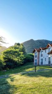 a large white house in a field with a hill in the background at Posada La Soñada in Villa General Belgrano