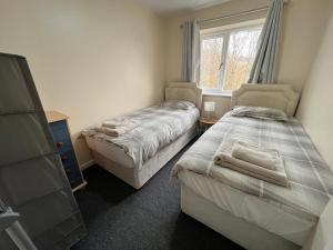 twee bedden in een kleine kamer met een raam bij Cosy 2 bedroomed semi detached house in Brettell Lane