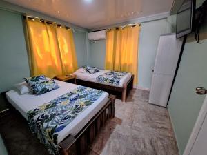two beds in a room with yellow curtains at Posada Cedar Valley in Providencia