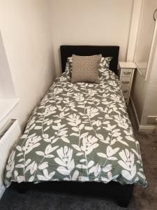a bed with a green and white comforter and a pillow at Ty Twt in Wrexham