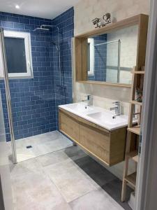 een badkamer met een wastafel, een spiegel en blauwe tegels bij Magnifique maison proche lac avec piscine chauffée in Sanguinet