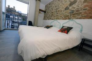 Una gran cama blanca en una habitación con una pared de piedra. en Hostel El Campano, en Villafranca del Bierzo