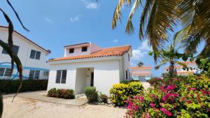 una casa blanca con flores y una palmera en Ocean Teal Villa Marazul en Westpunt