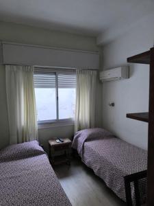 two beds in a room with a window at Hotel Lobato in Paysandú