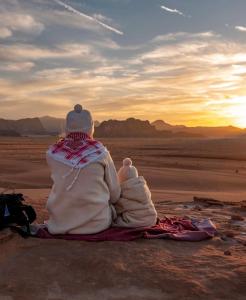 a person sitting in the desert watching the sunset at Bedouin desert life camp& Jeep tours in Wadi Rum