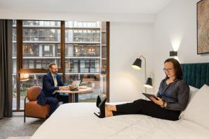 kobieta siedząca na łóżku w pokoju hotelowym w obiekcie The Sebel Canberra Campbell w mieście Canberra +44 zdjęcia