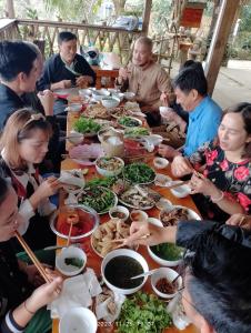 Un gruppo di persone seduti intorno a un tavolo che mangiano cibo di Cứ A Lồng Homestay a Bản Hon