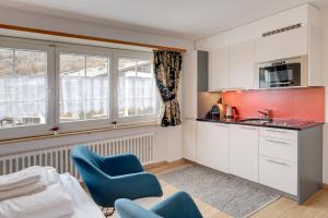 una cocina con armarios blancos, sillas azules y ventanas en Good Value Apartments by Mountain Exposure, en Zermatt