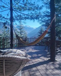 a hammock on a deck with a view of the mountains at Kudrat - A Boutique Homestay- Tirthan Valley in Banjār