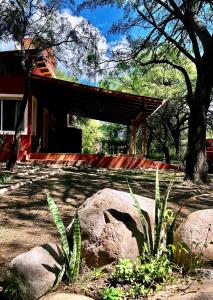 una casa roja con un árbol y algunas rocas en Casa bela energia en Villa Las Rosas