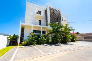 a white house with palm trees in a parking lot at CASA DUMAI OceanVilla NAKIJIN in Nakijin