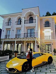 une femme debout à côté d'une voiture jaune devant une maison dans l'établissement Villa Trung Nghĩa 38, à Khu Chi Lăng
