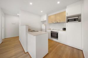 a white kitchen with white appliances and wooden floors at Comfy 1-Bed with Balcony in Tranquil Location in Weston Creek