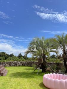 a yard with palm trees and a stone wall at On Stay Jeju in Jeju