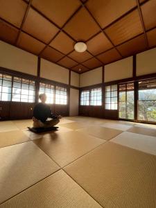 um homem sentado no chão numa sala com janelas em さぬきリトリート 繋安芯堂 em Kawashima