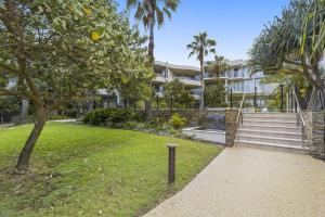 a building with a grassy yard with a tree and stairs at Cotton Beach on the Pool 66 in Casuarina