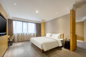 - une chambre avec un grand lit blanc et une télévision dans l'établissement Atour X Hotel Wuxi Sanyang Plaza Zhongshan Road, à Wuxi