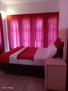 a bedroom with pink curtains and a bed and a couch at Bullez guest house in Mahikeng