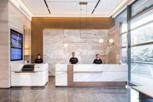 three people standing at a reception desk in a lobby at Atour Hotel Wuhan Chuhe Han Street Hongshan Plaza in Wuhan