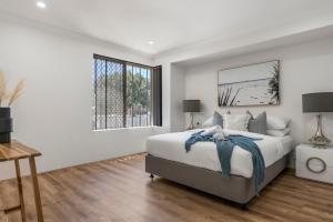 a white bedroom with a bed and a window at Coastal Charm: Halls Head Getaway in Mandurah in Mandurah
