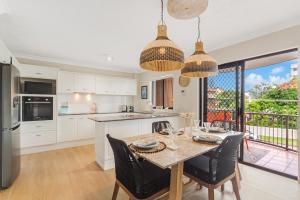 Bilinga Bliss - Luxury beachfront apartment في غولد كوست: مطبخ مع طاولة وكراسي ومطبخ مع دواليب بيضاء