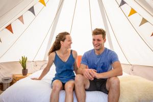 un homme et une femme assis sur un lit dans une tente dans l'établissement Boomkamp treehouses, à Oostkamp