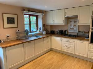 a kitchen with white cabinets and a wooden floor at Sweet Modern Country Cottage with Garden in Frome