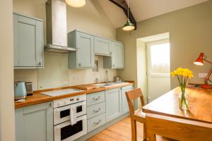 a kitchen with white cabinets and a table with yellow flowers at Tranquil 1 bedroom cottage 15 mins drive to sea in Mydroilin