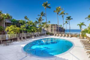 a swimming pool with chairs and the ocean in the background at Alii Villas 340 in Kailua-Kona