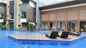 a swimming pool with two chairs in front of a building at Cozy Apartment Asatti Agate Yellow Vanya Park in Pagedangan