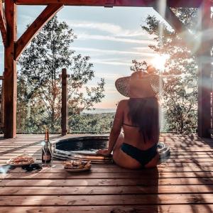een vrouw in bikini die op een terras naast een zwembad zit bij Cabanes du Hérisson, cabanes perchées de standing avec spa in Bonlieu