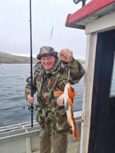 a man in camouflage holding a fish on a boat at Burtonport fishing trips in Dungloe