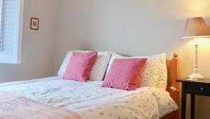 Una cama con almohadas rosas y blancas y una lámpara. en The Sanctuary, en Richmond