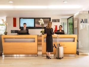 a woman standing at a reception desk with a suitcase at Mercure Paris Centre Tour Eiffel in Paris