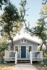 una casa blanca con una puerta azul y dos árboles en McKamy Cottage at Wrenwood Ranch, King Bed, en Johnson City