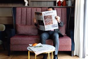 un hombre sentado en un sofá leyendo un periódico en Mode Paris Aparthotel, en París