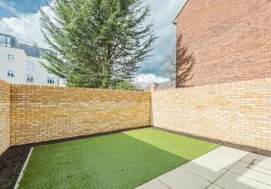 a brick wall with a green lawn next to a tree at Kings Mews Elegance: City Sparrow's Premier 2-Bedroom Residences in London