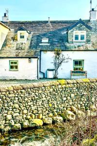 eine Steinmauer vor einem weißen Haus in der Unterkunft Cottage On The Brook in Keswick