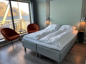 a bed in a room with two chairs and a large window at Værlandet Havhotell in Hamna