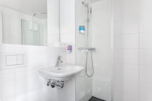 La salle de bains blanche est pourvue d'un lavabo et d'une douche. dans l'établissement Hotel Marta, à Zurich