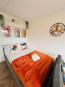 ein Bett mit einer orangenen Decke und einer Uhr an der Wand in der Unterkunft R2 - Private Room in Modern Shared Apartment, Each with Kitchenette, Central Birmingham in Birmingham