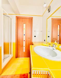 La salle de bains jaune est pourvue d'un lavabo et d'un miroir. dans l'établissement Hostdomus - Pietra Blu, à Pietra Ligure
