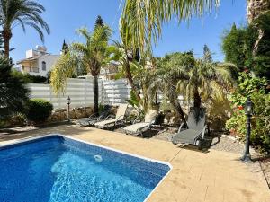 una piscina con 2 sillas y palmeras en Cheerful 3 bdr villa near the beach, en Bahía de Coral