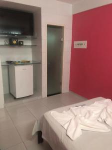 a room with a red wall and a bed and a kitchen at Pousada Ybyrápuan in Campina Grande