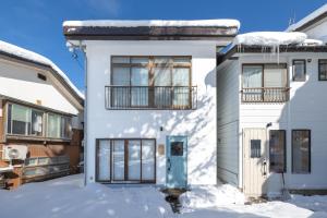 una casa blanca con una puerta azul en la nieve en Vaisala, en Nozawa Onsen