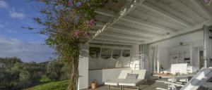 un patio con sillas blancas, una mesa y un árbol en Olivemare, en Katelios